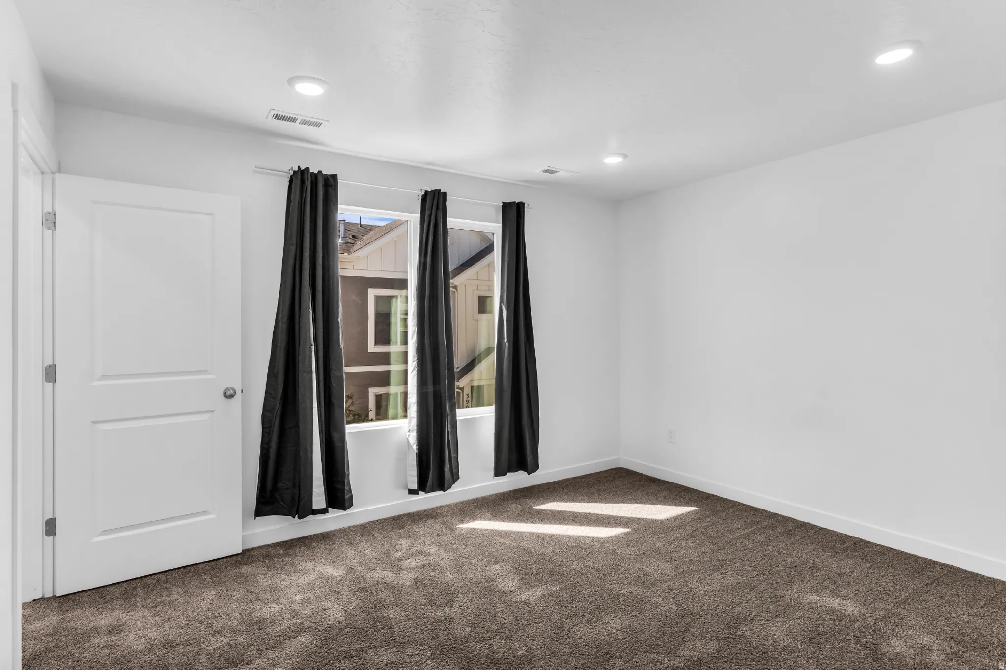 Recessed lighting, white walls, dark carpet, and a paneled white door