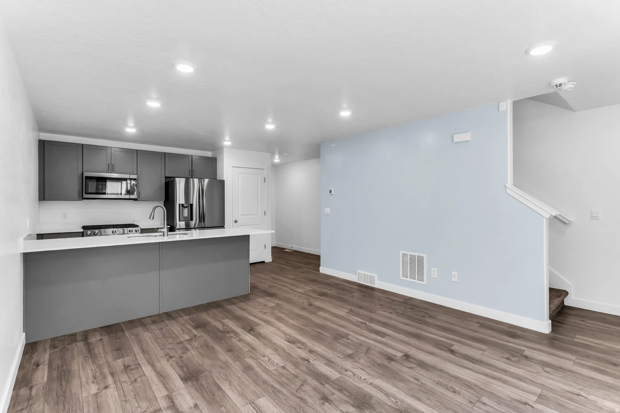 Modern kitchen with sleek gray cabinetry, stainless steel appliances, and a central island with white countertops