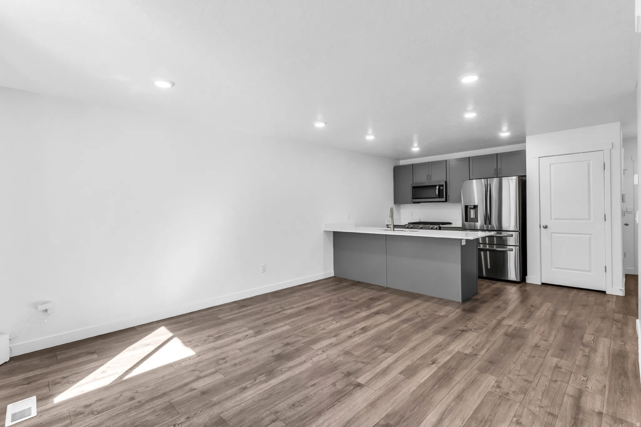 Open-concept living space featuring wood-finish flooring, recessed lighting, and a kitchen with gray cabinetry, a white countertop, and stainless steel appliances