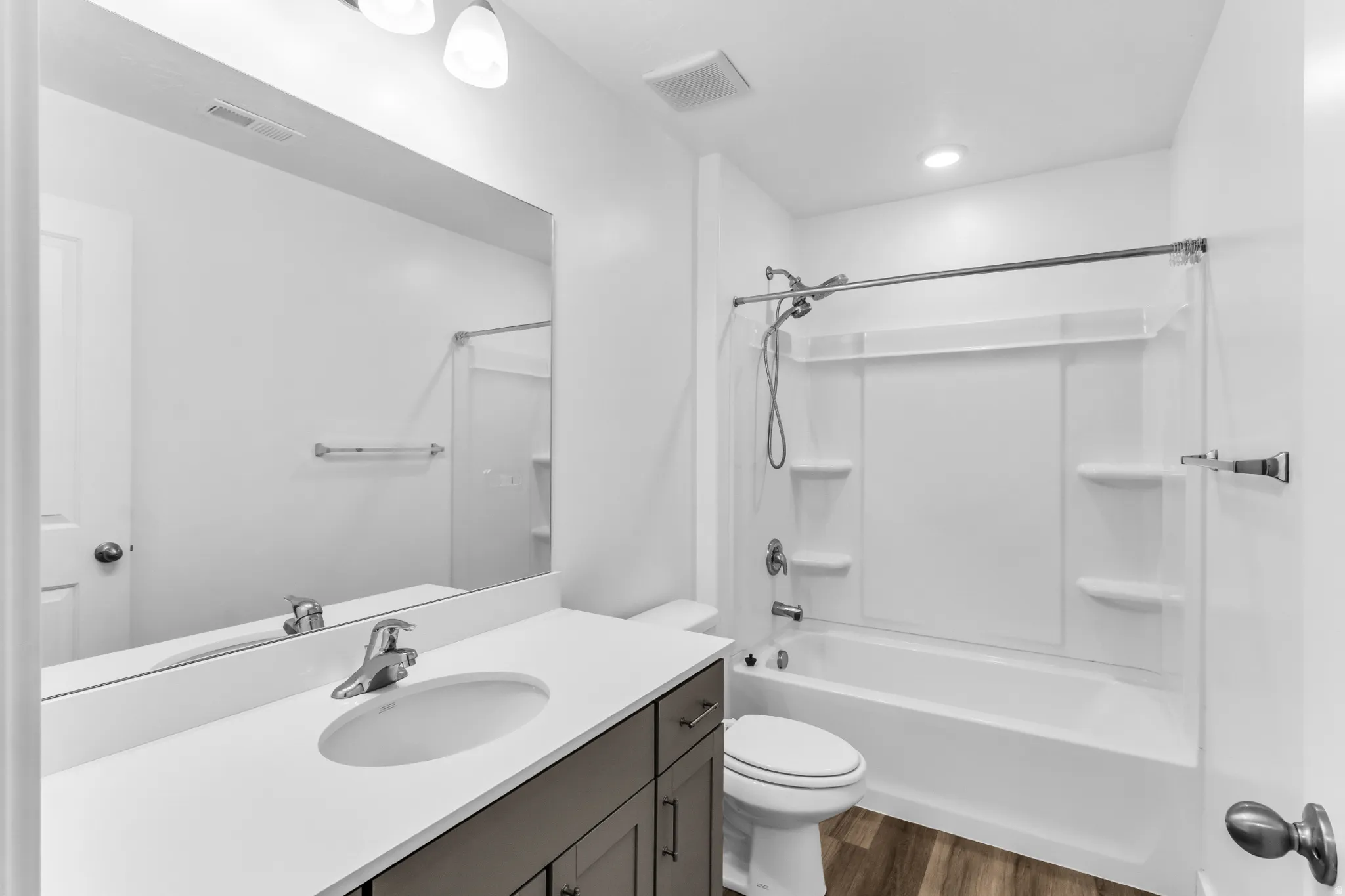 Vanity with integrated sink, expansive mirror, three-piece bathtub/shower combination, and wood-finish flooring