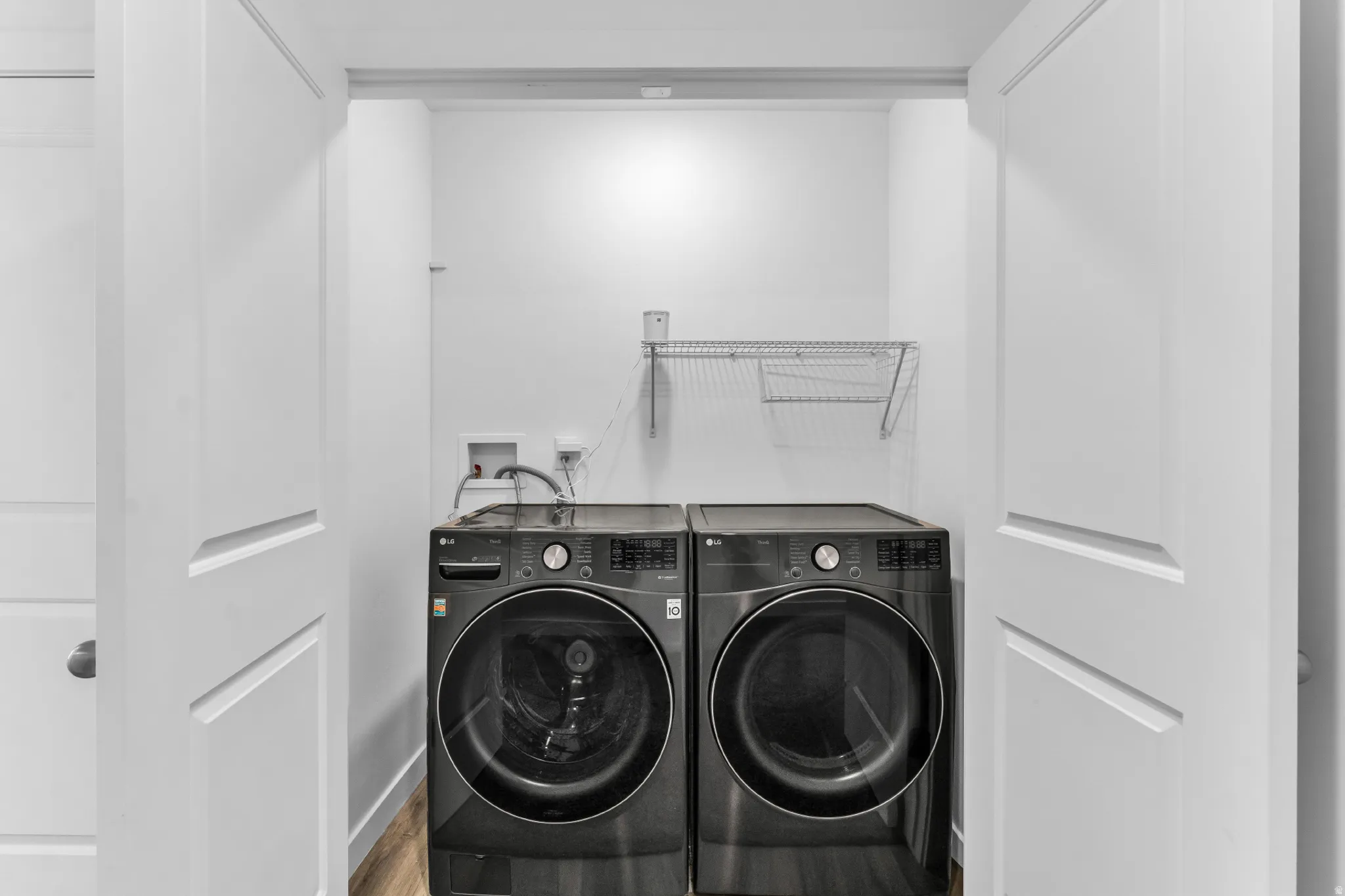 Dedicated laundry area with front-loading washer and dryer, wood-finish flooring, and wire shelving