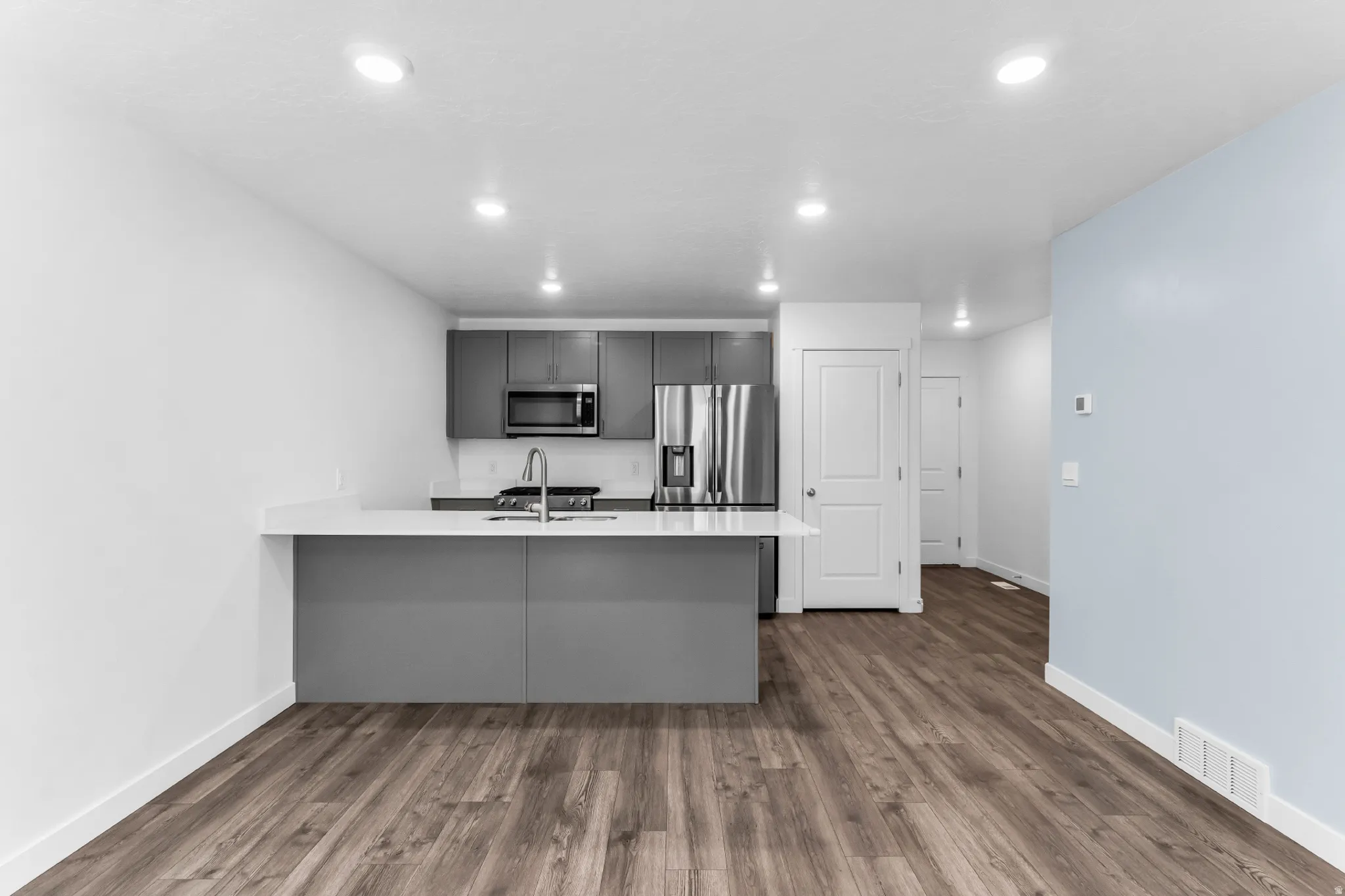 Modern kitchen featuring a large island with an integrated sink, white countertop, dark gray cabinetry, and stainless steel appliances
