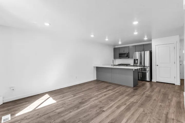 Open-concept living space featuring wood-finish flooring, recessed lighting, and a kitchen with gray cabinetry, a white countertop, and stainless steel appliances