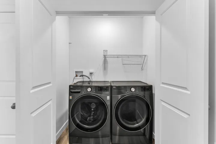 Dedicated laundry area with front-loading washer and dryer, wood-finish flooring, and wire shelving