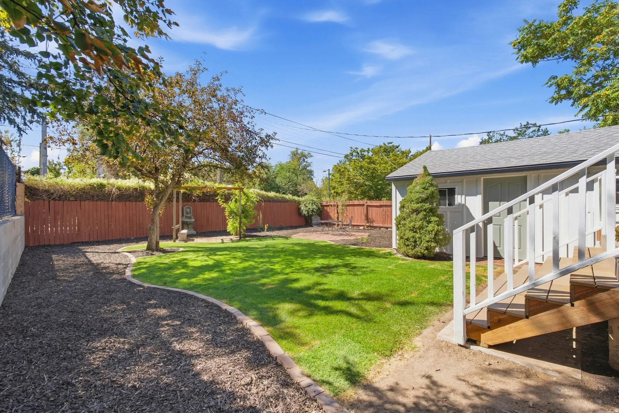 Manicured lawn, mature trees, wood fencing, garden shed, and wood deck with white railings