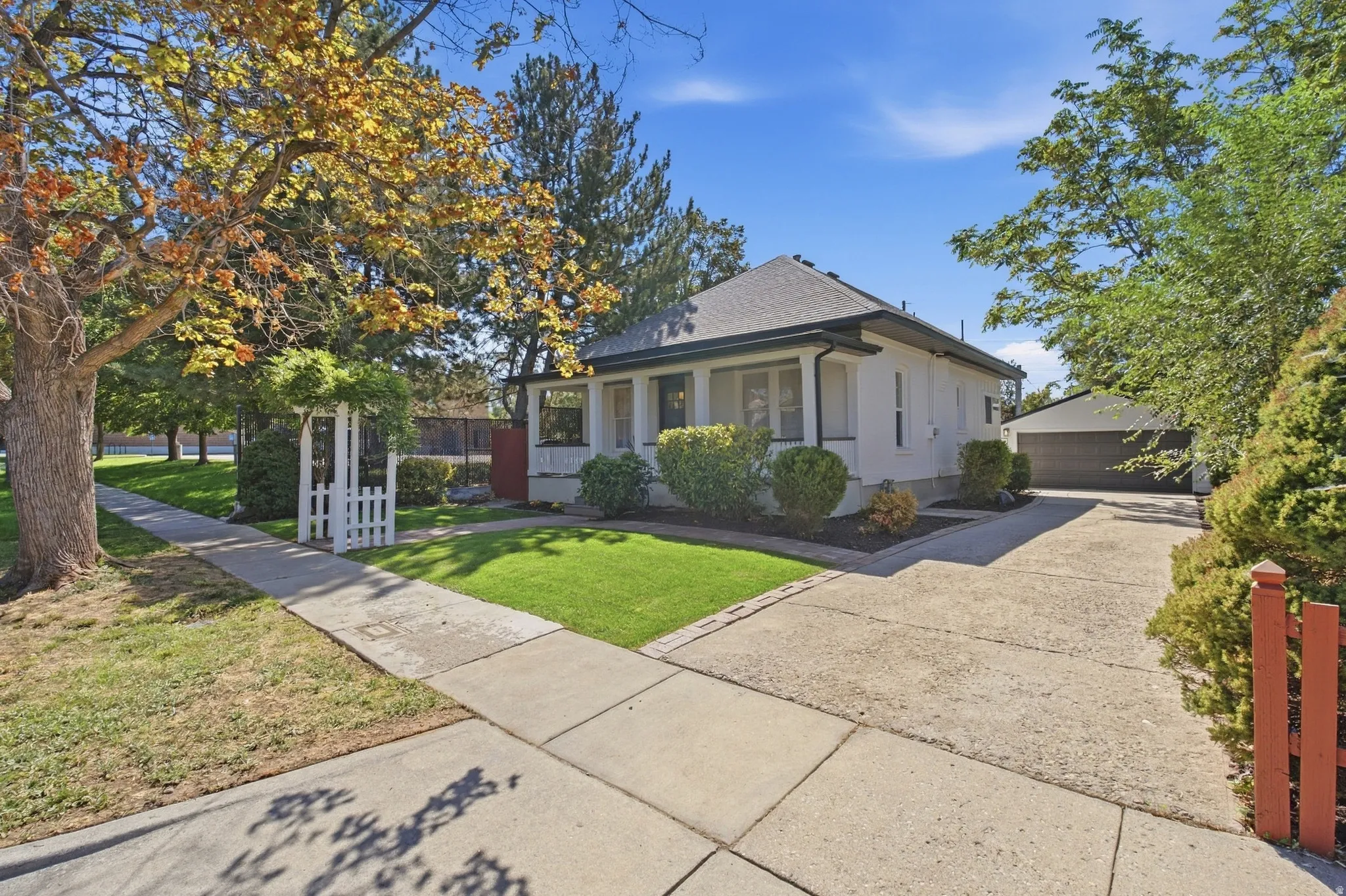 White exterior with dark trim, mature trees, manicured lawn, paved driveway, and detached garage