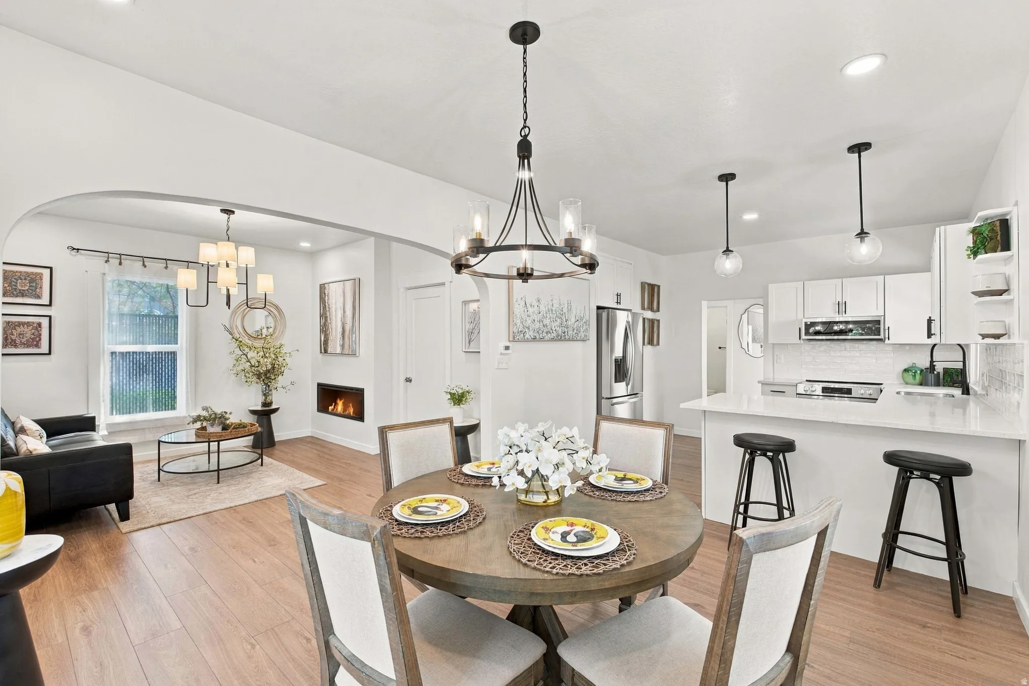 Open-concept living area featuring wood-finish flooring, a contemporary fireplace, and a kitchen with white cabinetry and a white subway tile backsplash
