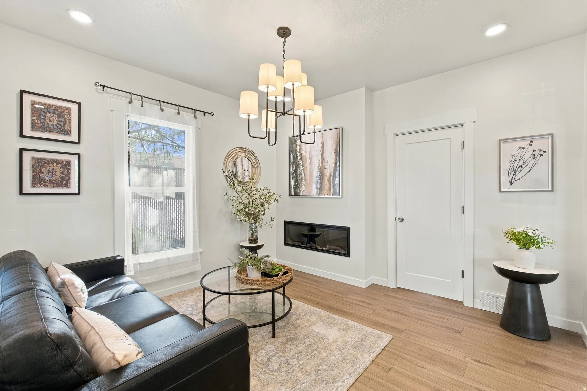 Recessed lighting and a modern chandelier illuminate this living space, featuring wood-finish flooring and a built-in fireplace