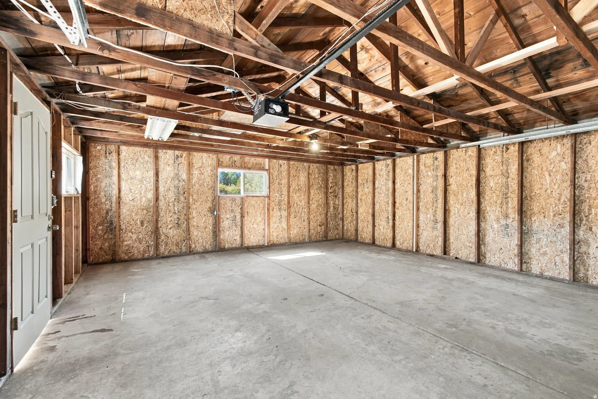 Spacious garage with exposed wood rafters, concrete flooring, and multiple windows allowing natural light