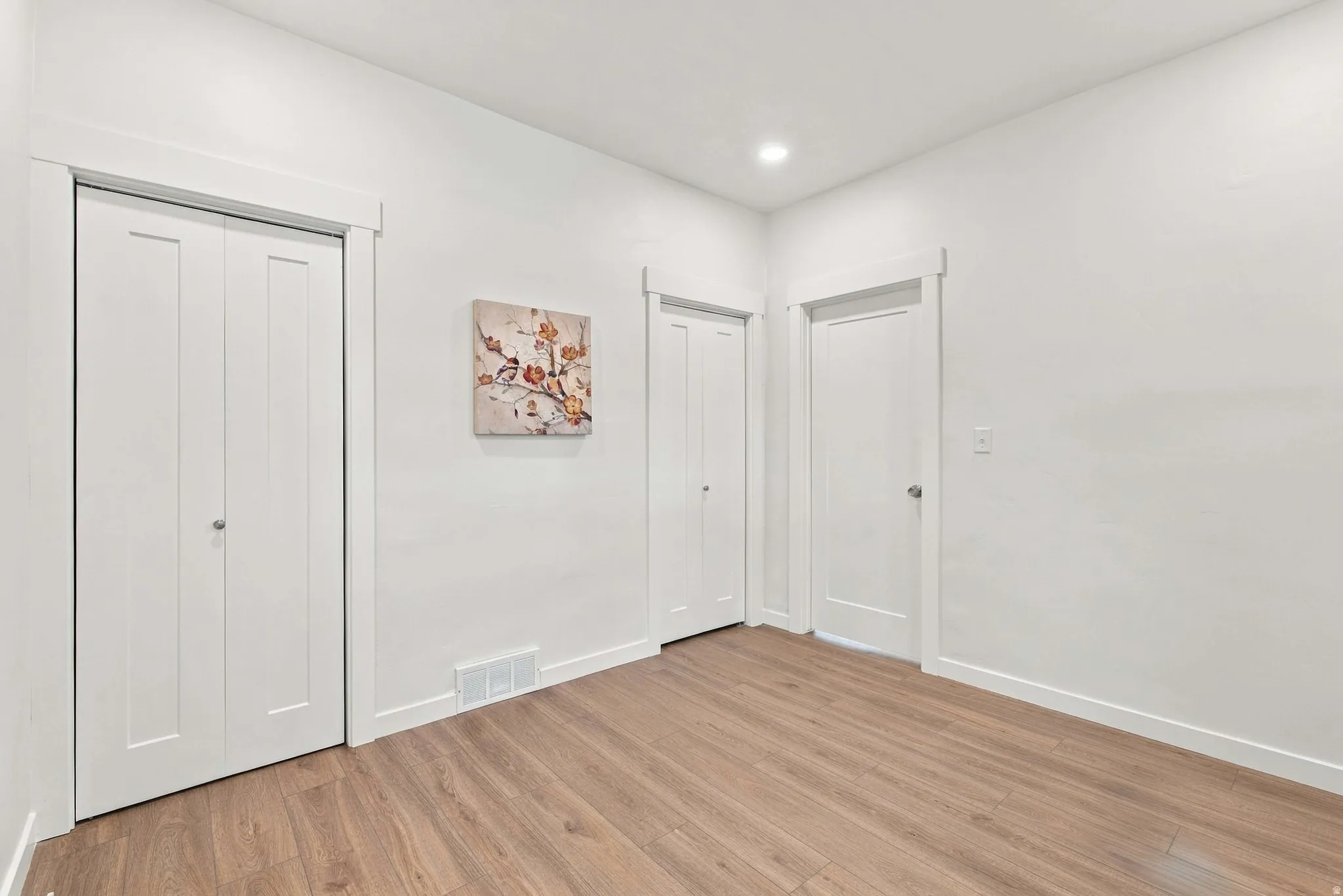 Wood-finish flooring, white walls, recessed ceiling lighting, and white trim