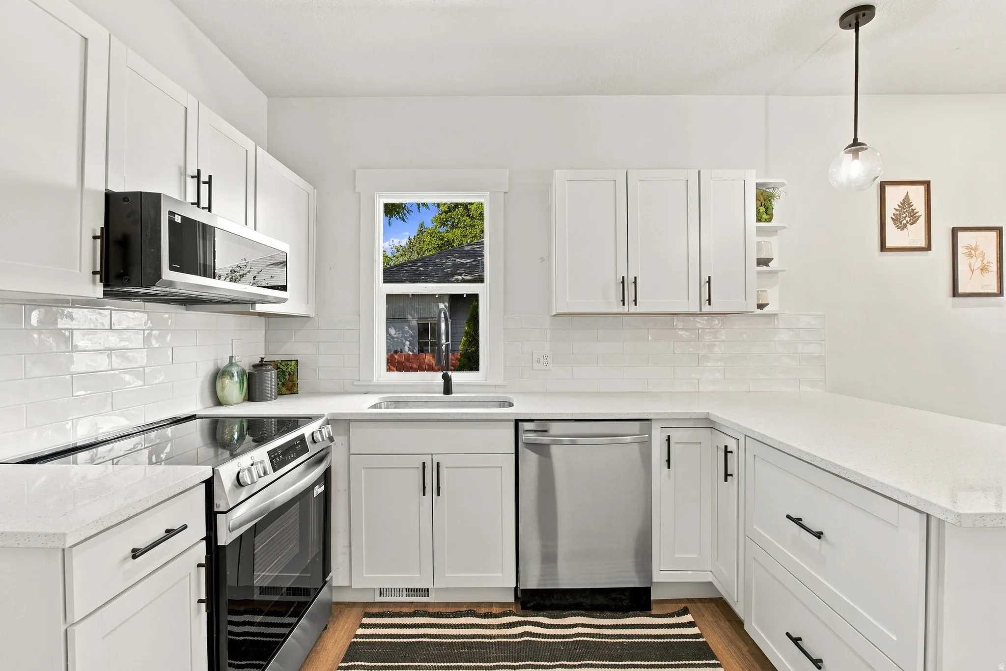 White shaker cabinetry with black hardware, stainless steel appliances, quartz countertops, white subway tile backsplash, and wood-finish flooring