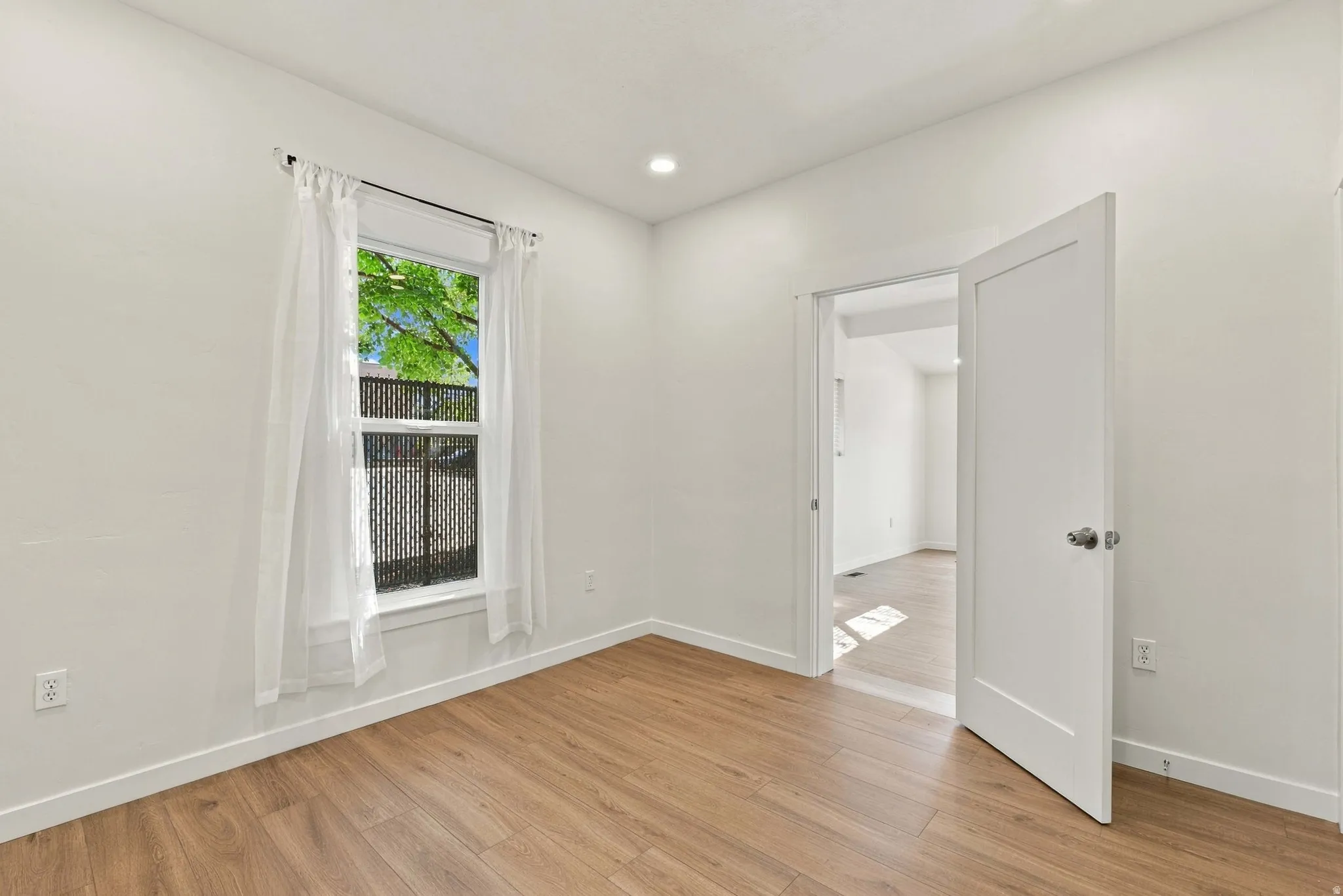 Wood-finish flooring, recessed lighting, and a white interior door with a modern handle