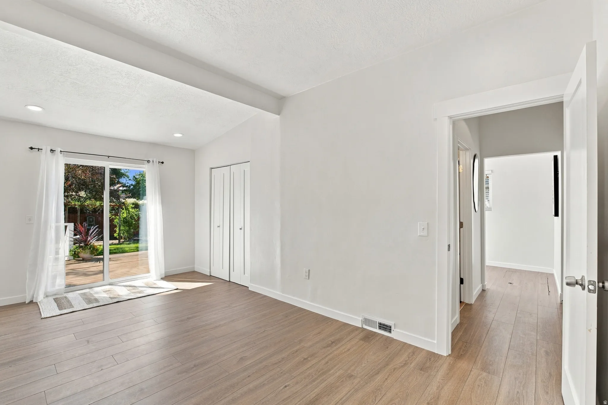 Vaulted ceiling with recessed lighting, wood-finish flooring, sliding glass patio door, and bi-fold closet doors