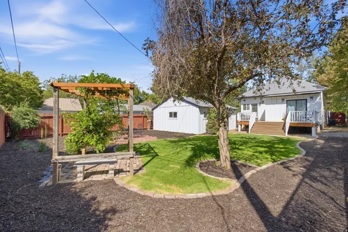 Expansive backyard featuring a wood pergola with built-in seating, a detached shed, and a raised wood deck with white railings and sliding glass door access