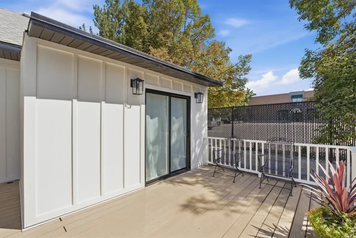 Private balcony with composite decking, white board-and-batten siding, black trim, and a sliding glass door