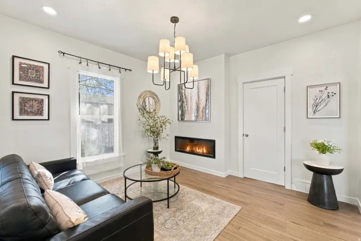 Recessed lighting, wood-finish flooring, and a contemporary chandelier illuminate this space featuring a built-in electric fireplace and a white interior door