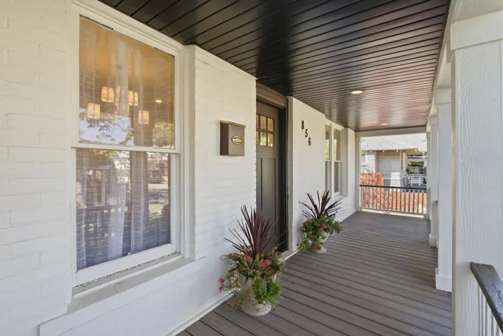 Covered front porch featuring a dark wood-finish ceiling, white brick facade, and dark wood-finish decking