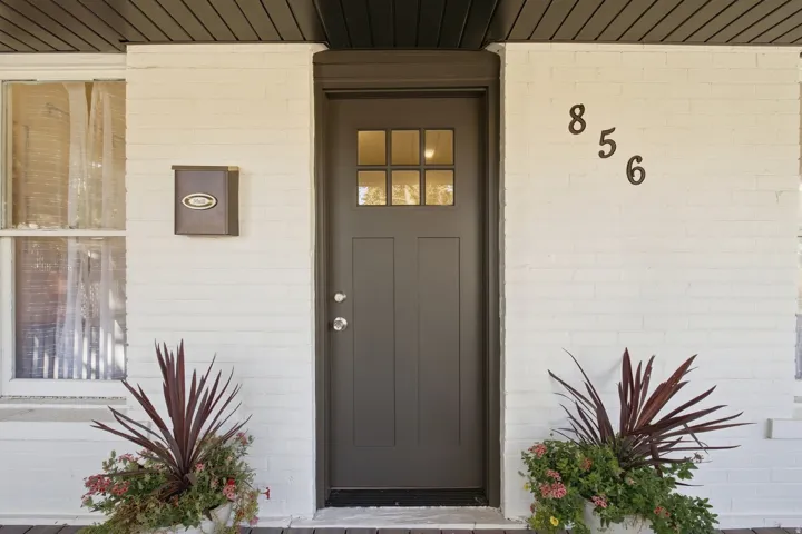 Painted brick exterior with a dark-paneled front door, transom window, and prominent house numbers