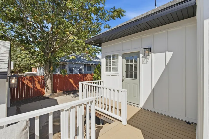 White board and batten exterior, wood-finish decking, white railing, gray paneled door, and exterior sconce lighting