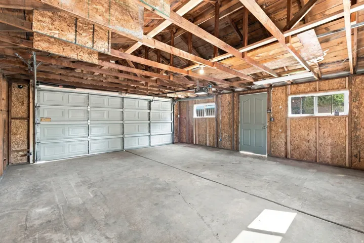 Spacious garage featuring a concrete floor, exposed wood beam ceiling, two windows, and a side access door