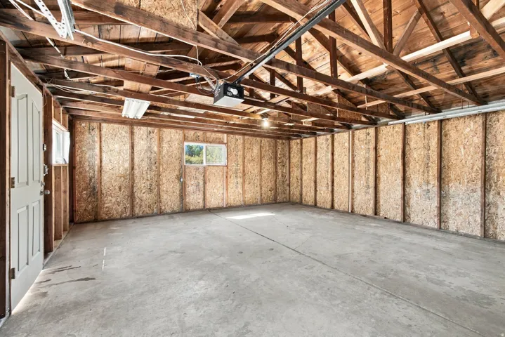 Spacious garage with exposed wood rafters, concrete flooring, and multiple windows allowing natural light