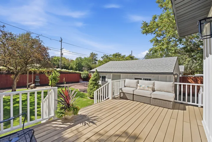Expansive outdoor deck with white railing, overlooking a lush green lawn and secondary structure