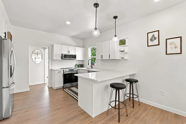 Kitchen featuring white cabinetry, light-toned countertops, stainless steel appliances, and wood-finish flooring