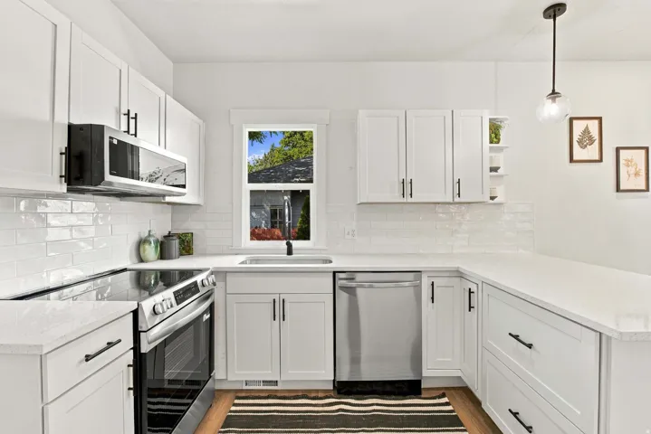 White shaker cabinetry with black hardware, stainless steel appliances, quartz countertops, white subway tile backsplash, and wood-finish flooring