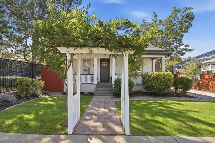 Inviting front entry with brick paver walkway and a white pergola adorned with greenery