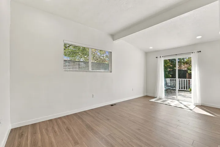 Wood-finish flooring with white walls, a window featuring horizontal blinds, and sliding glass doors opening to an outdoor patio