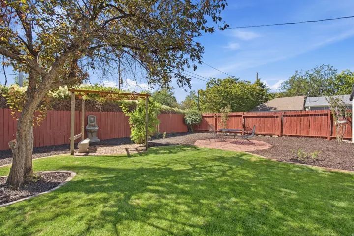 Expansive lawn with mature shade tree, brick paver patio, wood privacy fencing, and a decorative arbor with a built-in fountain
