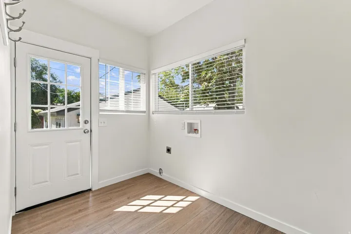 White walls, wood-finish flooring, multiple windows with blinds, a glass-paned door, and laundry hookups