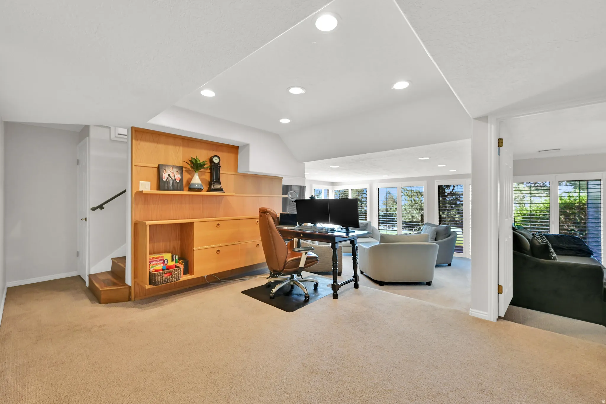Recessed lighting, wood-finish built-in shelving, carpet flooring, multiple windows, and a staircase with a handrail