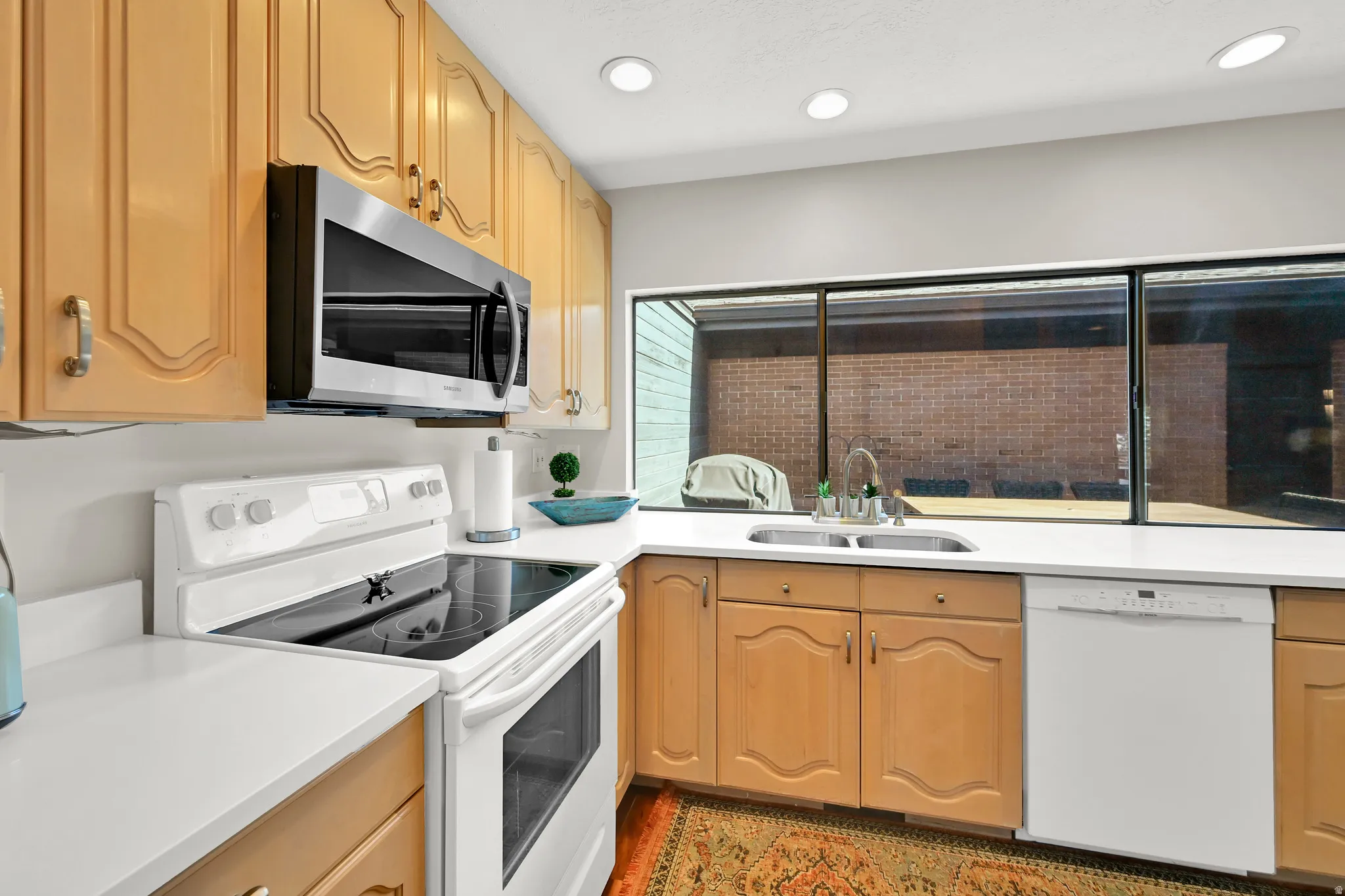Kitchen featuring wood cabinetry, white countertops, stainless steel microwave, white electric range, and a dual-basin stainless steel sink