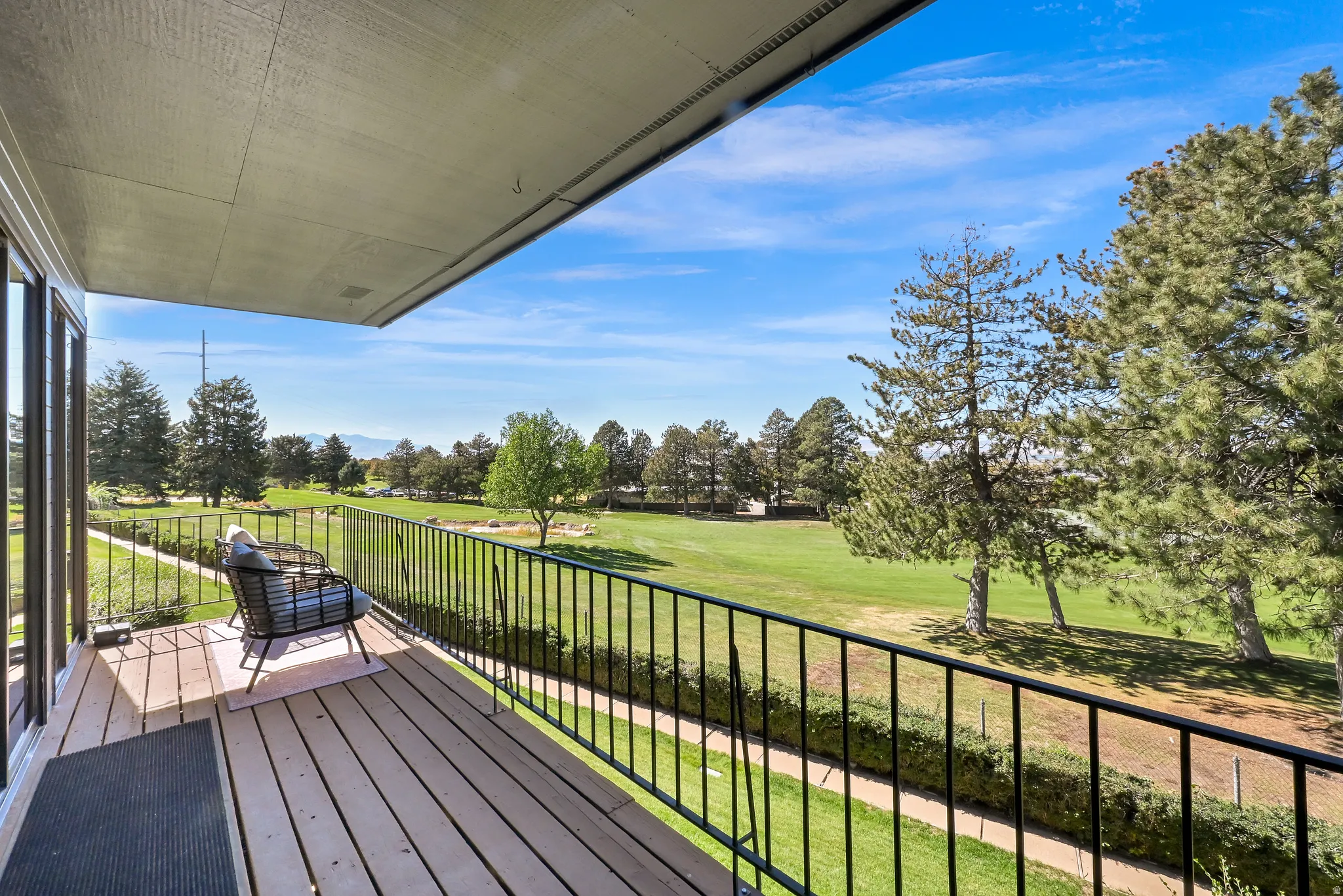 Private balcony with wood-finish decking and black metal railing overlooking a landscaped green space