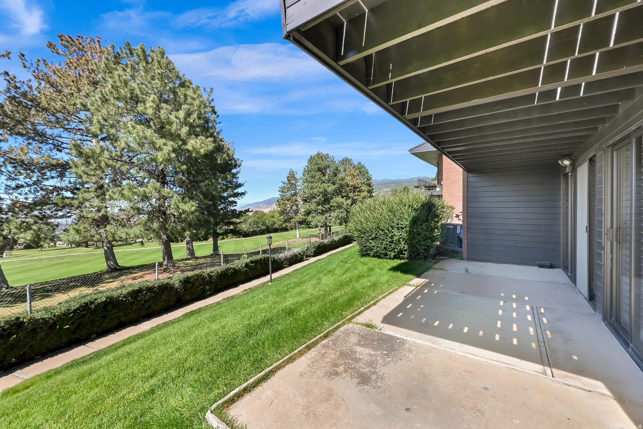 Concrete patio with overhead covering, expansive green space, mature trees, and landscaping bordering a golf course