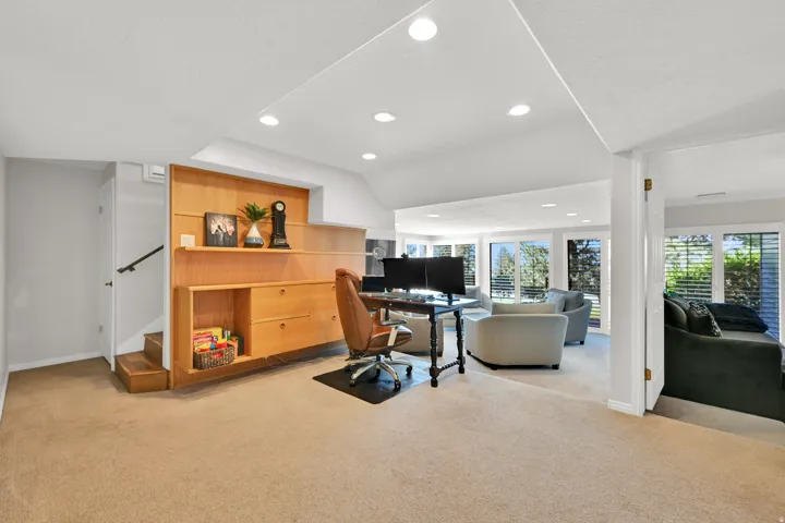Recessed lighting, wood-finish built-in shelving, carpet flooring, multiple windows, and a staircase with a handrail