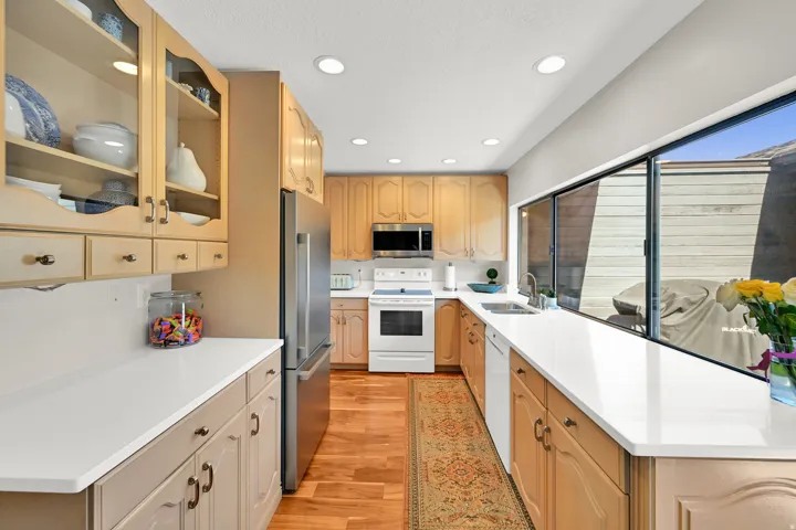 Galley kitchen with wood-finish flooring, light-toned cabinetry, stainless steel refrigerator, white countertops, and recessed lighting
