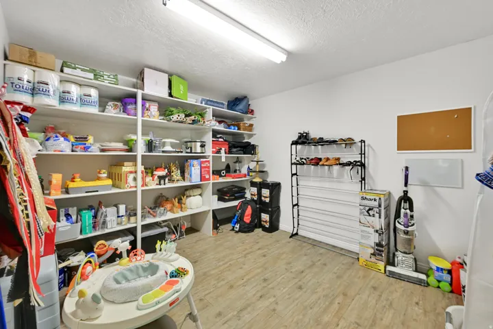 Wood-finish flooring with extensive wall-mounted shelving, overhead fluorescent lighting, and white painted walls
