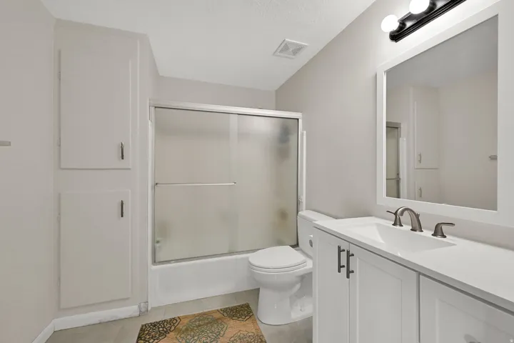 White vanity with an integrated sink and brushed nickel faucet, framed mirror, and a shower-tub combination with a sliding glass door