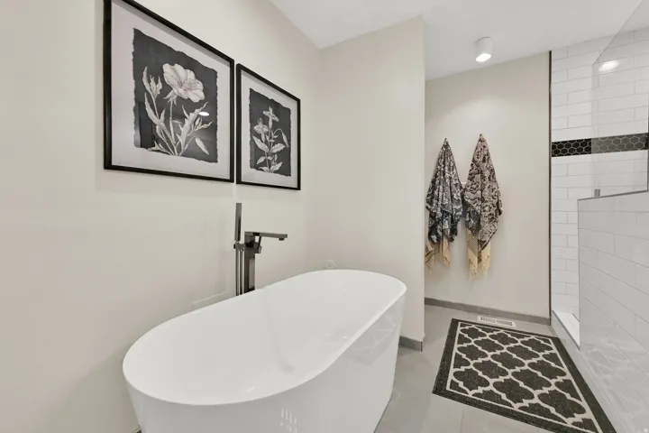 Freestanding soaking tub with floor-mounted faucet, walk-in shower with subway tile, and a decorative black hexagon tile accent