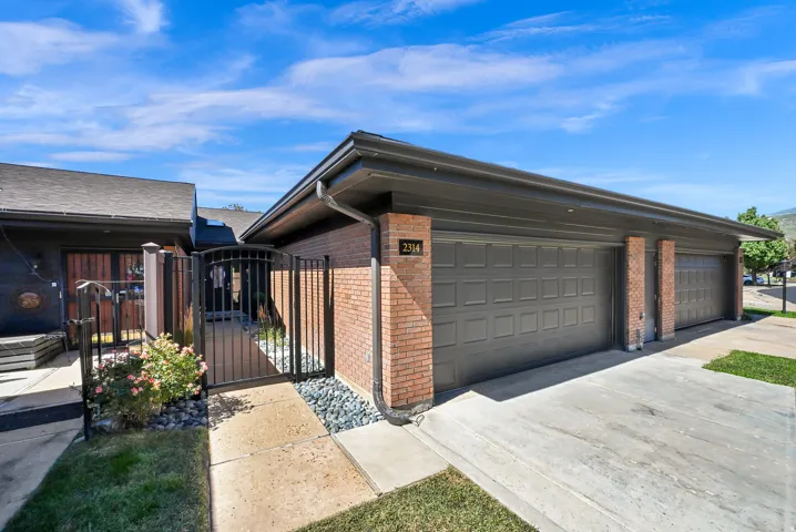 Brick facade with dual garage doors, black wrought iron gate, concrete pathway, and landscaping with decorative river rock