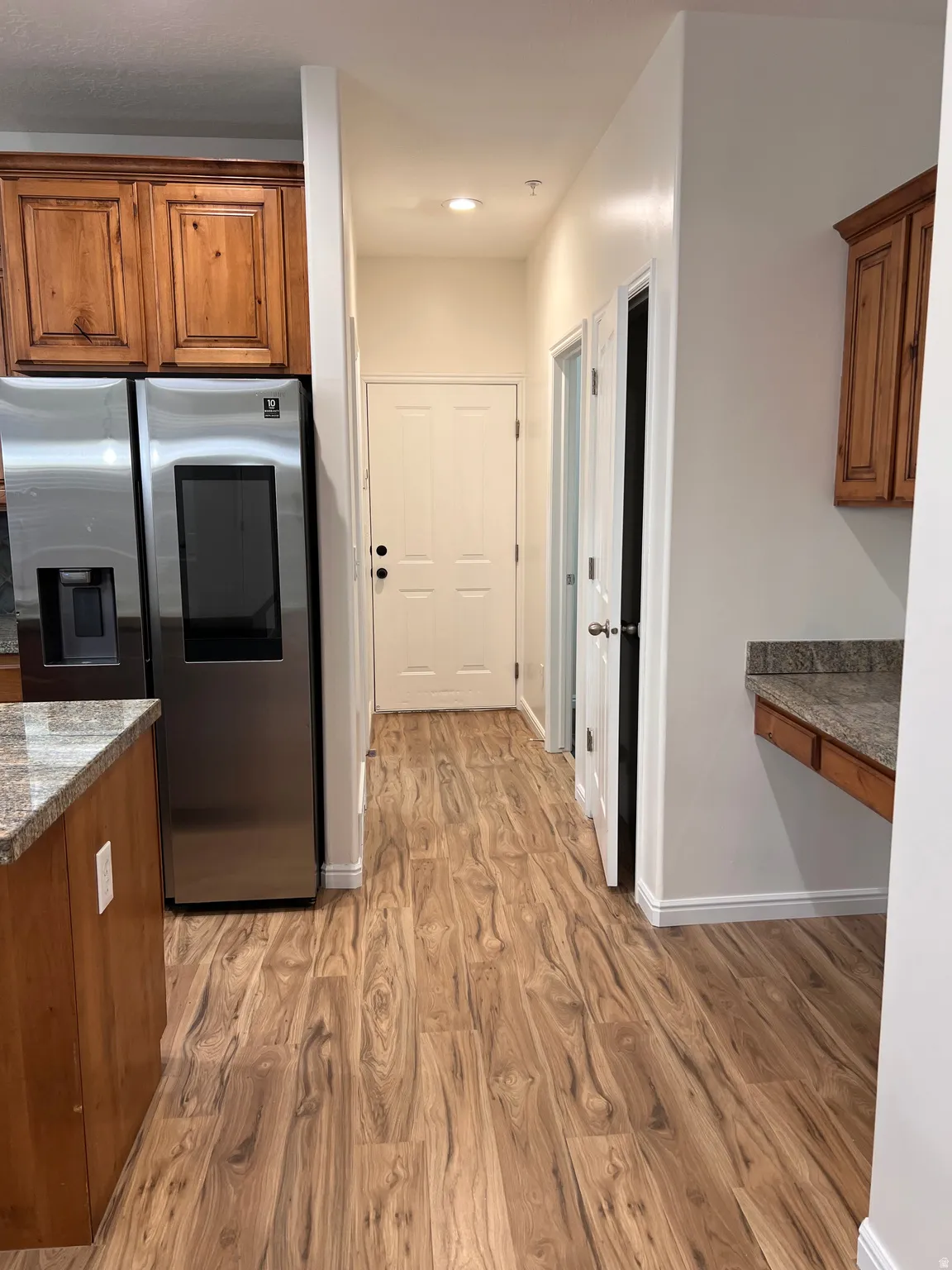 Modern kitchen featuring stainless steel French-door refrigerator with ice and water dispensers, wood cabinetry with granite countertops, and wood-finish flooring throughout