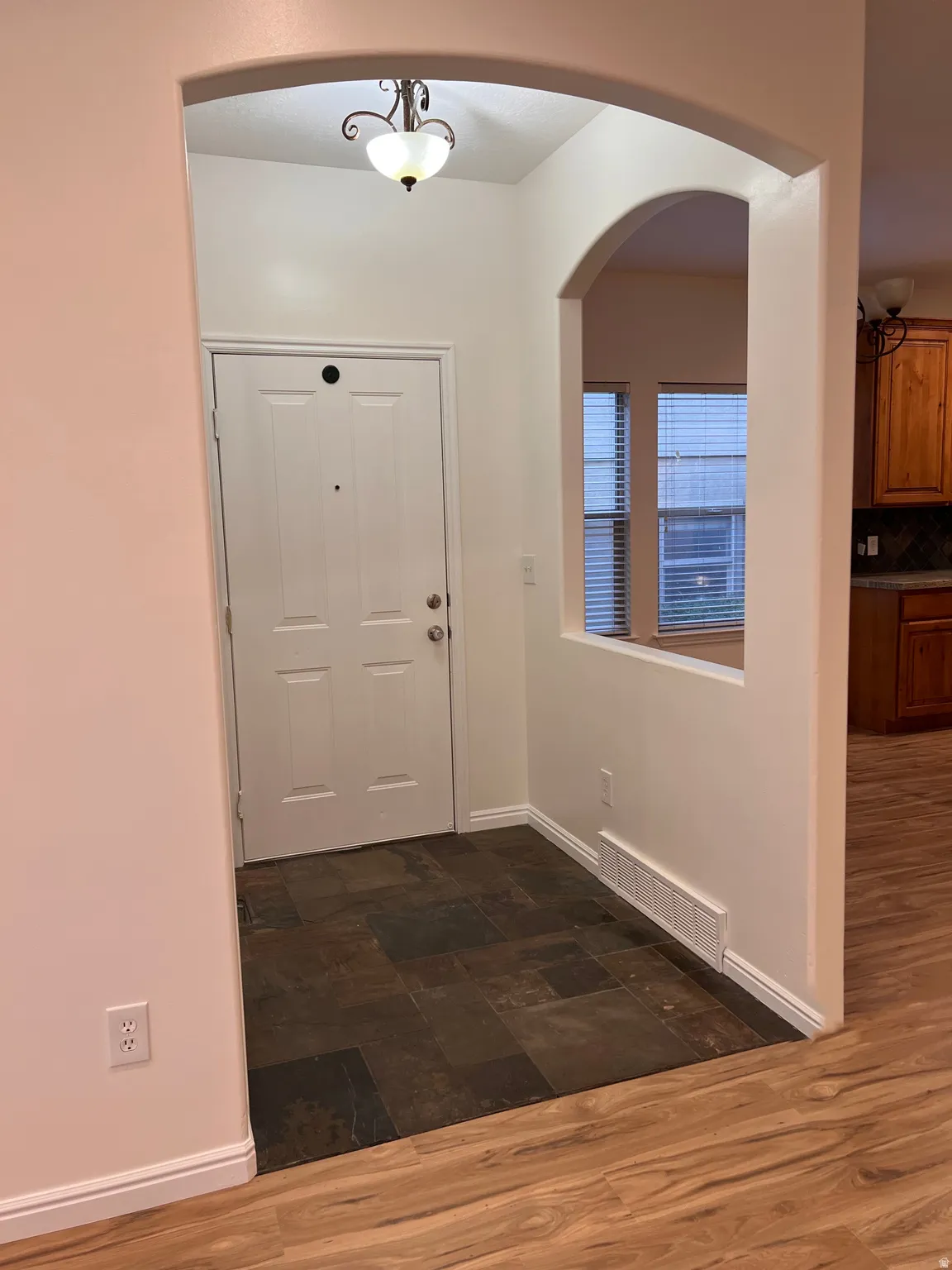 Arched entryway with a decorative ceiling fixture, wood-finish flooring, and slate-style tile