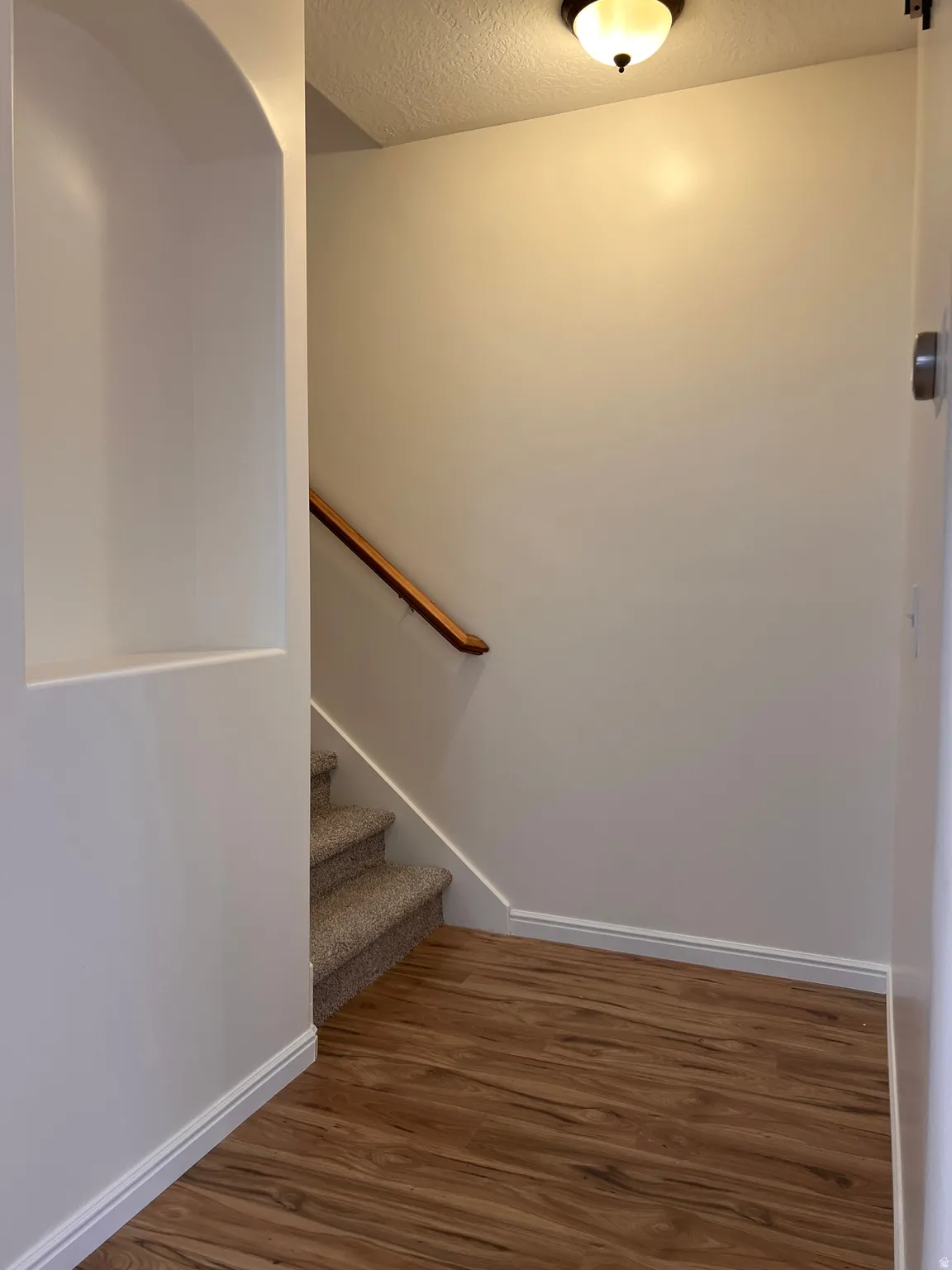 Wood-finish flooring, staircase with carpeted treads, wood handrail, recessed wall niche, and flush mount lighting