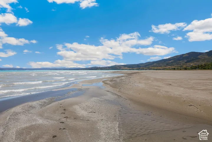 Expansive sandy beach with a vast water body, distant mountainous terrain, and a clear blue sky