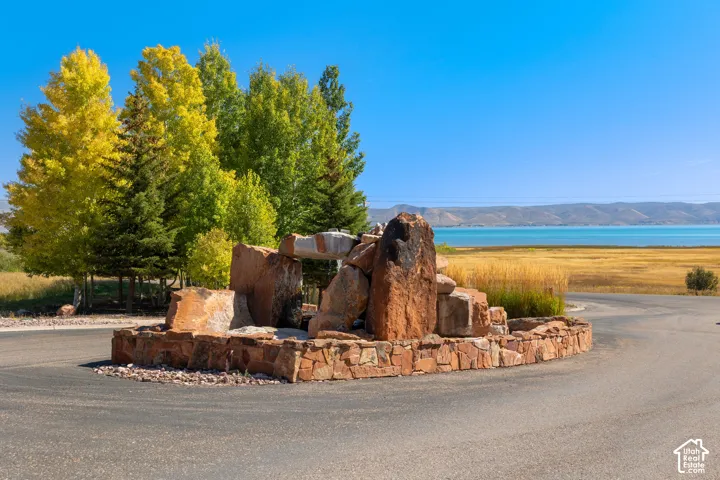 Stone water feature with a stone base, surrounded by mature trees, and a distant body of water