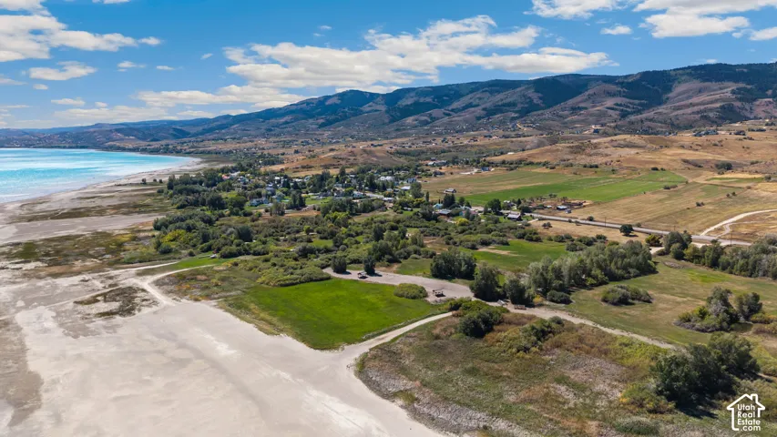 Expansive shoreline with turquoise water, surrounded by mountainous terrain, green fields, and clusters of mature trees