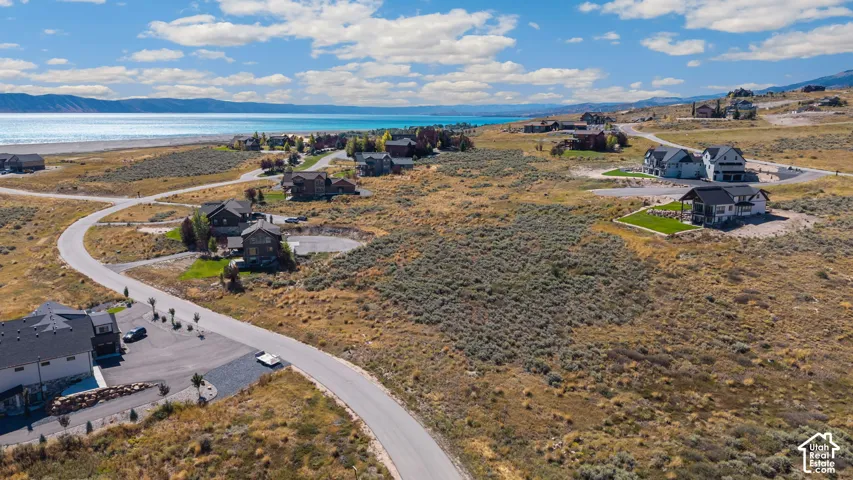 Expansive land parcel featuring natural shrubbery and a paved road, situated on a hillside with distant water and mountain scenery