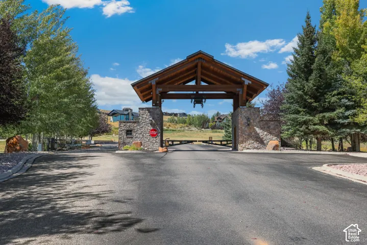 Stone and timber entrance structure with a gabled roof, paved asphalt driveway, and mature landscaping